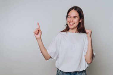 Asyalı genç bir kadın minimalist bir çevrede kutlama yapıyor ve yukarı doğru işaret ediyor.