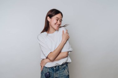 Sıradan giyinmiş gülümseyen genç bir kadın sade bir arka planda mutluluğun tadını çıkarıyor.