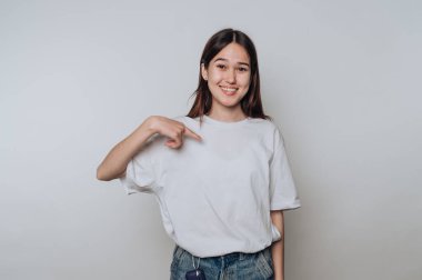 Gülümseyen Asyalı genç kadın, gündüz saatlerinde iç mekan ortamında gömleğini işaret ediyor.