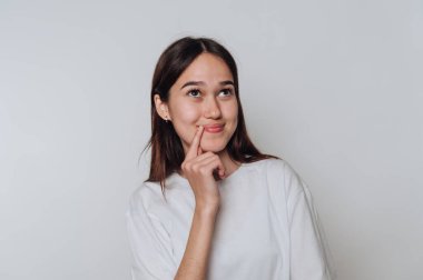 Genç Asyalı kadın, gündüz vakti ev ortamında sade bir arka planda düşünceli bir şekilde düşünüyor.