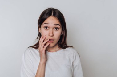 Genç Asyalı kadın, doğal bir ortamda sade bir arka plan karşısında dururken şaşkınlığını dile getiriyor.