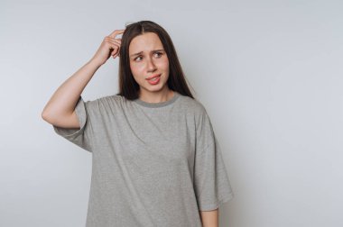 Tarafsız bir arka planda günlük bir ortamda kafa karışıklığını ifade eden genç bir kadın.