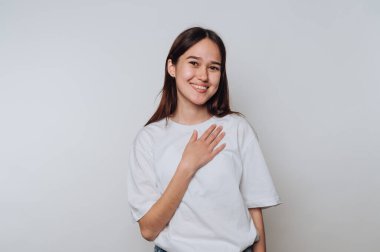 Genç bir kadın gülümsüyor ve el ele hareket ediyor. Tarafsız bir arka plana karşı. Kapalı bir alanda.