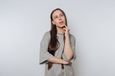 Düşünceli genç bir kadın hafif bir arkaplan karşısında neşeli bir ifadeyle bir fikir düşünüyor.