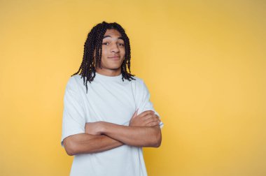 Örgülü saçları olan genç bir kız, sıradan bir fotoğraf çekimi sırasında parlak sarı bir arka plana karşı güvenle poz verir.