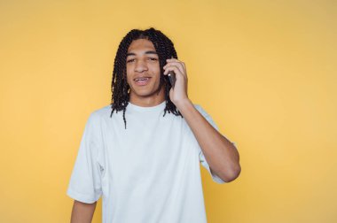 Genç adam neşeli bir sohbete gülümserken parlak sarı bir arka planda telefonda konuşuyor.