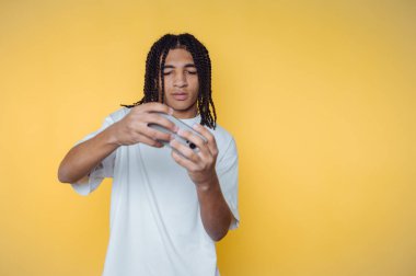 Örgülü saçı olan bir genç, akıllı telefonuyla şehir ortamında parlak sarı bir arka planda etkileşim kuruyor.