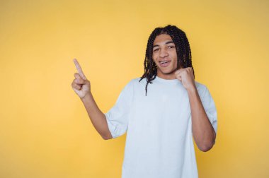 Parlak sarı bir arka planda neşeli bir şekilde kutlama yaparken gülümseyen ve coşkuyla el kol hareketi yapan genç bir adam.