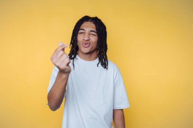 Sıradan giyinmiş, gülümseyen ve parlak sarı bir fon karşısında jest yapan Afro-Amerikan genç bir adam.