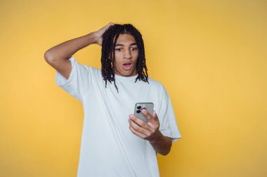 Şaşırmış genç adam, akıllı telefonundan gelen beklenmedik haberlere, parlak sarı bir arka plana tepki veriyor.