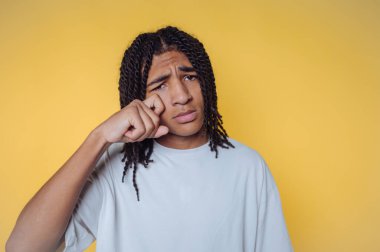 Saçları örgülü genç bir adam parlak sarı bir arka plana karşı düşünceli bir yüz ifadesi sergiliyor.