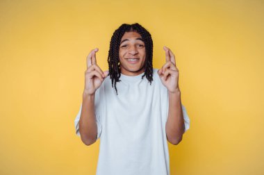 Saçları örgülü genç bir Afrikalı şans dilemek için şans diliyor. Parlak bir stüdyoda sarı arka planda.