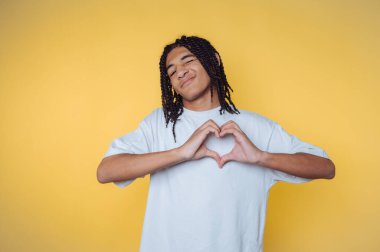 Genç Afrikalı bir adam elleri ile kalp şeklini oluşturur parlak sarı bir arka plan, neşe ve pozitiflik ifade eden eğlenceli, gündelik bir ortam