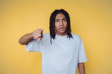 Parlak sarı bir arka plana işaret ederken saçları örgülü genç adam şaşkınlığını dile getiriyor.