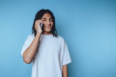 Açık mavi arka planda rahat bir ifadeyle telefonda konuşan genç bir adam.