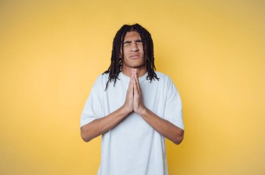 Minnettarlığını, parlak sarı bir arkaplan önünde ellerini sıkarak ifade eden genç bir adam.