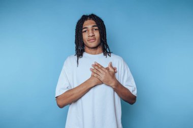 Örgülü saçlı genç, mavi bir arkaplana karşı, arkadaşça bir ifadeyle güvenle poz veriyor.