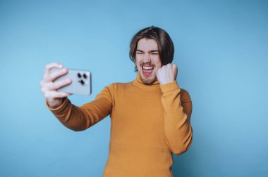 Genç adam, renkli bir odada kişisel başarısını kutlarken heyecanlı bir şekilde selfie çekiyor.