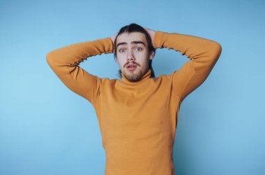 Açık mavi bir arkaplan önünde gelişigüzel bir anda şaşkınlığını ifade eden genç adam.