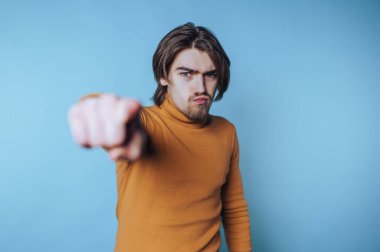 Uzun saçlı genç adam, özgüvenini ifade eden, mavi bir arka plana karşı özgüvenli bir şekilde hareket eder.