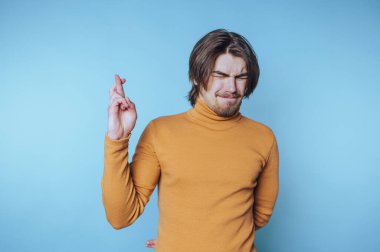 Parmakları çapraz genç adam açık mavi bir arka plana karşı umutlarını ifade ediyor.