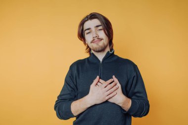 İçerideki parlak sarı arka plana karşı elleri yüreğinde şükranlarını ifade eden genç bir adam.