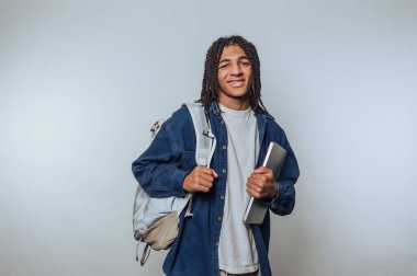 Gülümseyen genç öğrenci dizüstü bilgisayar ve sırt çantası tutuyor.