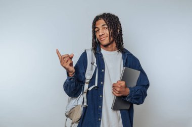 Bilgisayarlı ve sırt çantalı öğrenci, kapalı alanda güvenle poz veriyor.