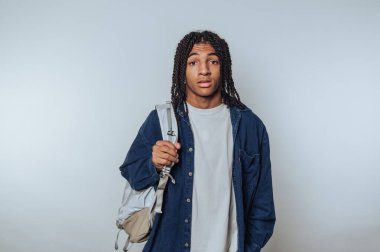 Saçları örgülü genç Afrikalı bir adam sırt çantasıyla güvenle ayakta duruyor.