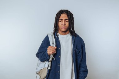 Saçları örgülü genç bir adam. Sırt çantasını kapalı alanda tutuyor.