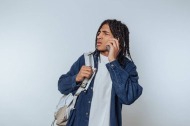 Sırt çantalı genç adam kapalı alanda arka planda akıllı telefonla konuşuyor.