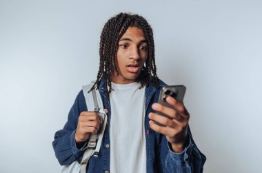 Sırt çantalı genç adam evde akıllı telefonunu kontrol ederken şaşırmış görünüyor.