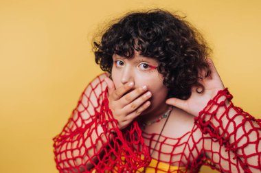 Yaratıcı ifade, kıvırcık saçlı, parlak kırmızı örgü bir üst giyen birinin parlak sarı bir arka plana karşı durduğunu gösteriyor.