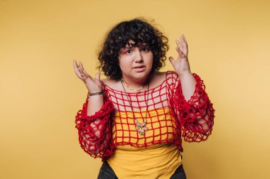 Genç bir kadın, stüdyo ortamında yaratıcı bir fotoğraf çekimi sırasında parlak sarı bir arkaplan karşısında şaşkınlığını dile getiriyor.