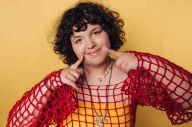 Yaratıcı portre oturumunda parlak kıyafetli genç, sarı arka plana karşı neşeli bir ifade sergiliyor.