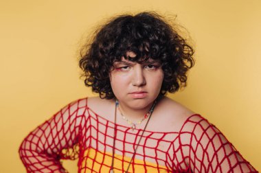 Parlak sarı arka planda kıvırcık saçlı, renkli kıyafetler giyen bir kişinin portresi.