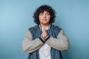 Kapalı bir alanda mavi bir arka planda dururken umut ve minnettarlığını ifade eden genç bir adam.