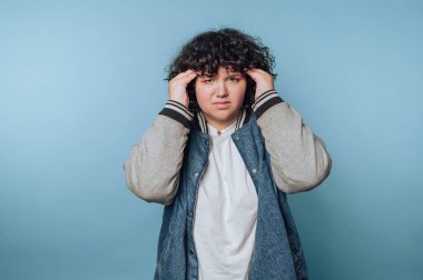 Mavi bir arka plan karşısında günlük kıyafetlerle hayal kırıklığını ifade eden genç bir insan stresli bir anda duygusal bir ifade sergiliyor.