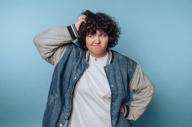 Kıvırcık saçlı, mavi bir arkaplan önünde sıradan bir iç mekan anı boyunca kafa yoran meraklı biri.