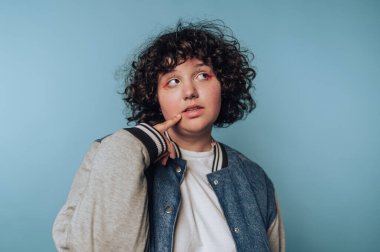 Kot ceketli genç adam özenle mavi bir arkaplanda poz veriyor.