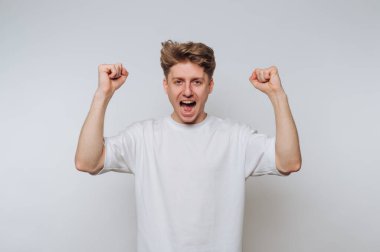 Heyecanlı genç adam başarısını parlak, minimalist kapalı mekan ortamında yumruklarını kaldırarak kutluyor.