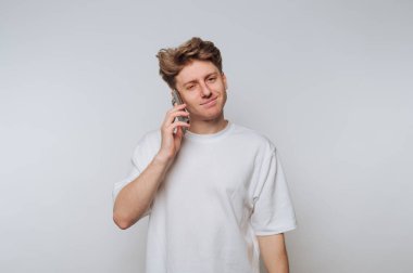 Genç adam telefonda konuşuyor. Tarafsız bir arkaplan ortamında sıradan bir ifadeyle.