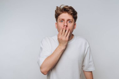 Genç adam şaşkınlığını açık renkli bir ortamda elleri ve ağzı açık bir şekilde gösteriyor.