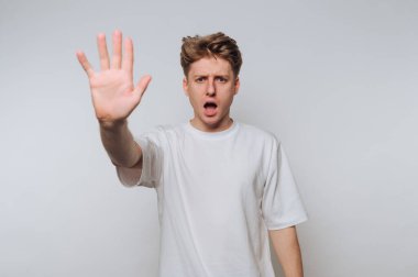 Şok olmuş ifadesi olan genç adam, minimalist bir mekanda kapalı kalmak için el kaldırıyor.