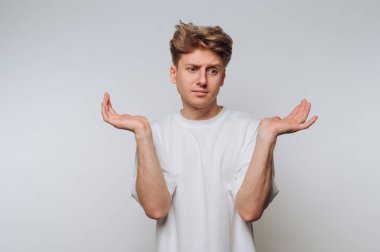 Kafası karışmış genç bir adam, beyaz bir arkaplanda dururken belirsizliğini ifade ediyor.
