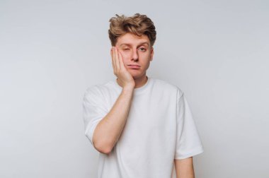 Genç bir adam, sıradan bir ortamda yüzüne dokunarak hayal kırıklığını ifade ediyor.