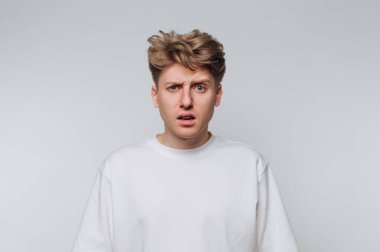 Kafası karışmış, saçları dağınık bir genç adam, sıradan bir iç mekan anında sade bir arka fonda dikiliyor.