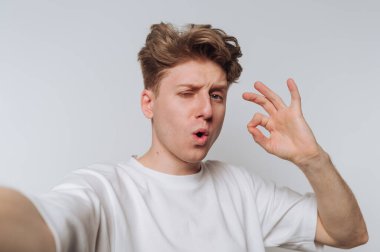 Genç adam basit bir iç mekanda selfie çekerken iyi bir jest yapıyor.