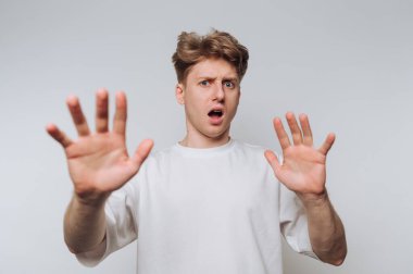 Şaşırmış yüzlü bir adam beyaz bir arka plana karşı sürpriz bir hareketle el kaldırır.