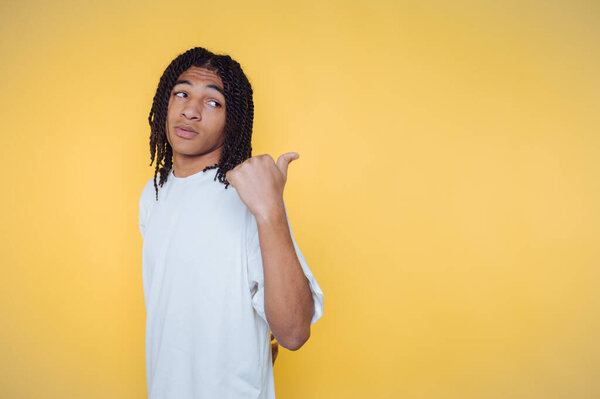 Молодой человек с плетеными волосами позирует на ярко-желтом фоне, демонстрируя игривое выражение лица